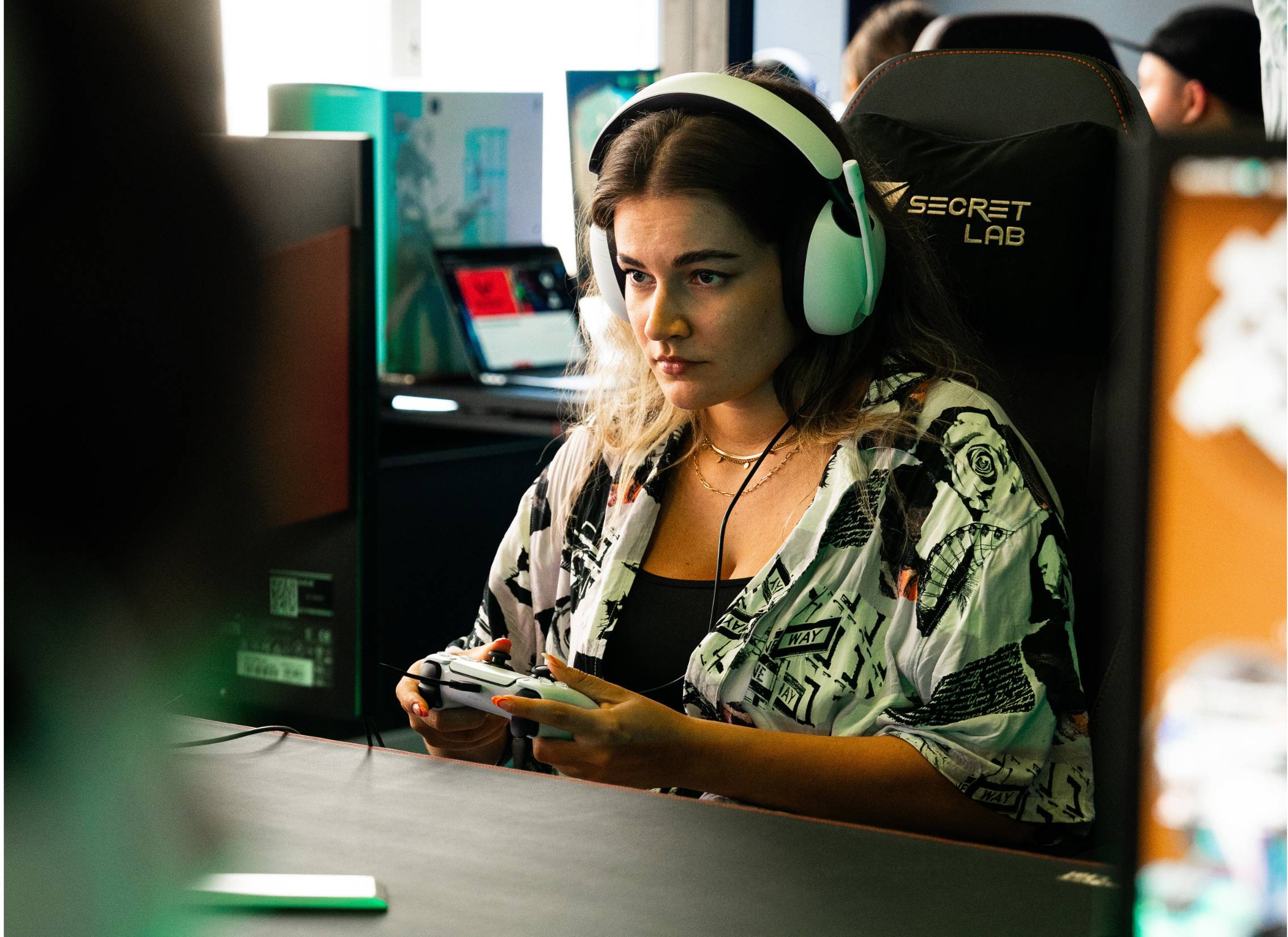 Eine blonde Gamerin mit Headset auf dem Kopf und einer geblümten Bluse konzentriert sich auf ihr Videospiel.