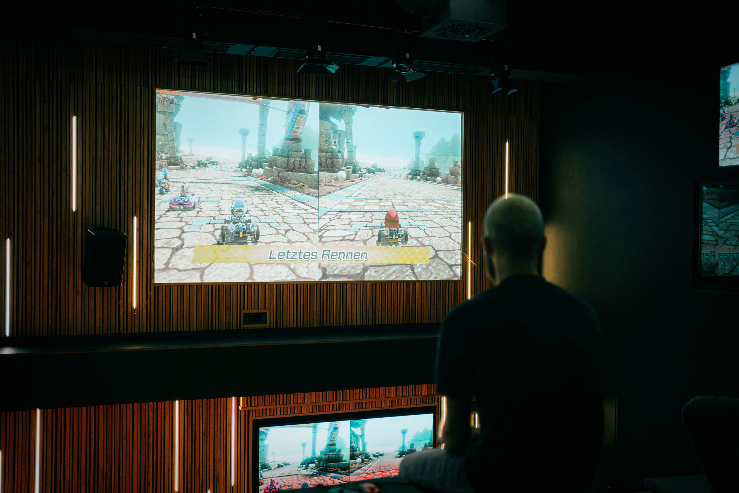 r42_gaming_causal-konsolen Großer Bildschirm in der Eventarena auf dem Mario Cart gespielt wird.