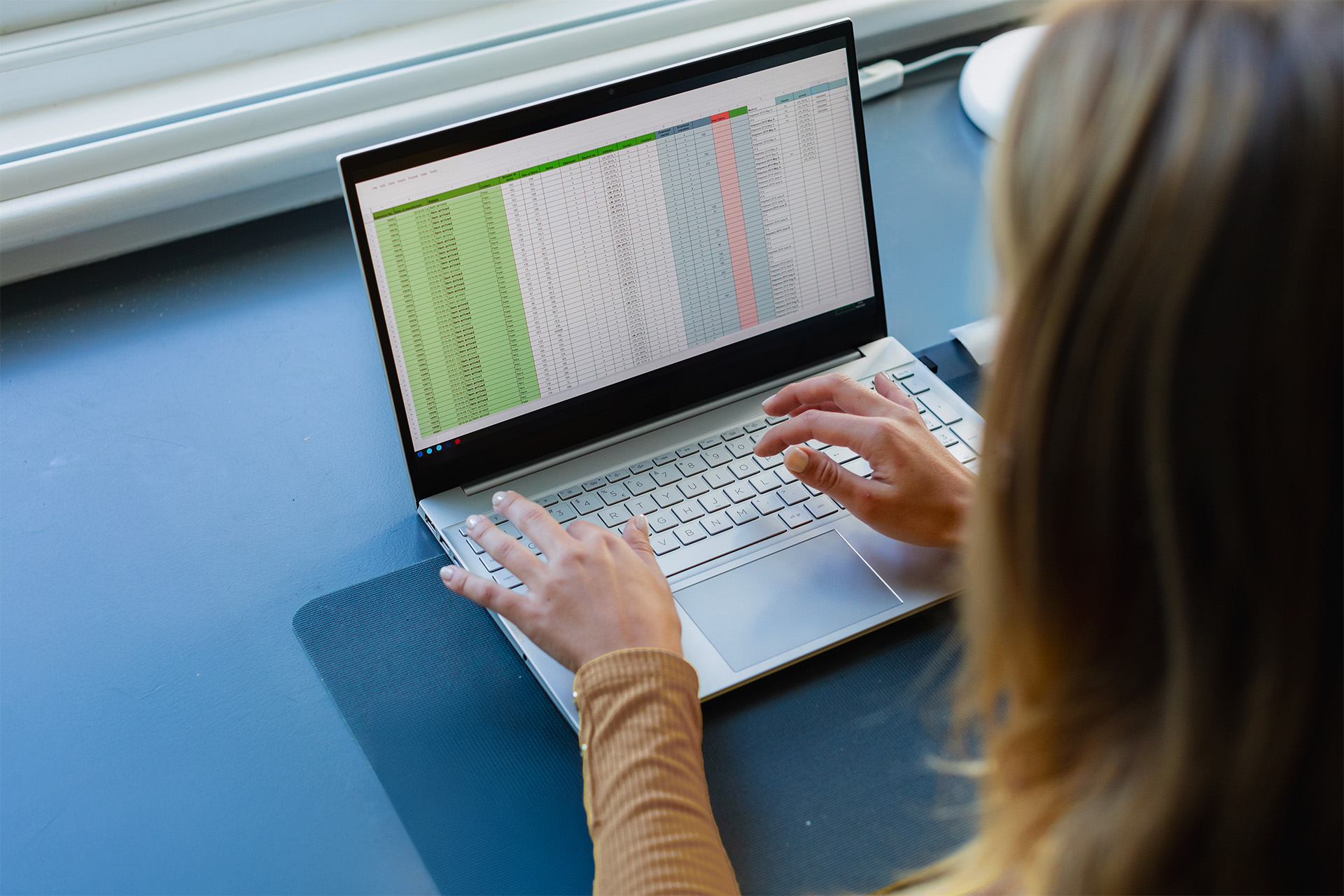 Eine Person arbeitet an einem Laptop mit einer geöffneten Excel-Tabelle, die farblich markierte Daten in Spalten zeigt.
