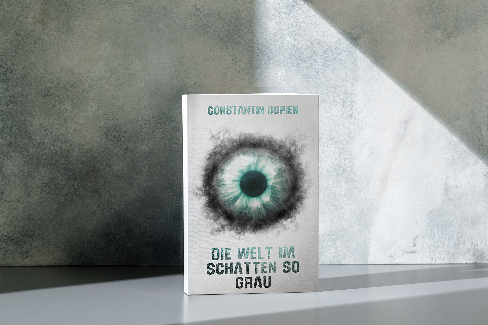 Das Buch "Die Welt im Schatten so grau" von Constantin Dupien. Das Cover ist weiß. Darauf ist mittig ein großes Auge zu sehen. Von der dunklen Pupille aus wird die Iris erst türkisblau bis weiß und läuft nebelartig schwarz aus. Über dem Auge steht Constantin Dupien in türkisblauer Schrift. Unter dem Auge steht der Buchtitel in einem türkisblau schwarzen Farbverlauf.