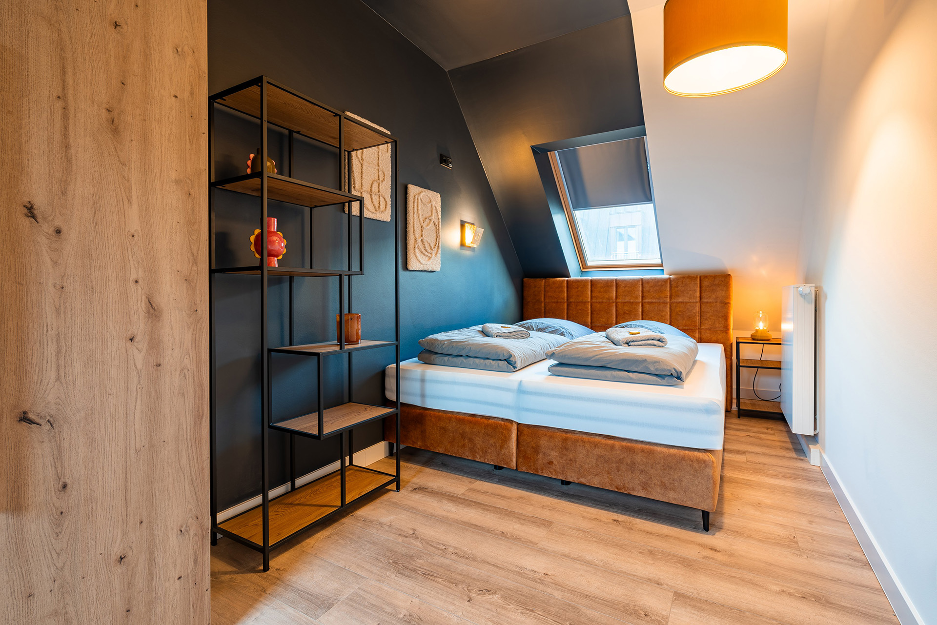 Modern eingerichtetes Apartment namens Lara's Loft im R42 in Leipzig, gemütlichem Schlafzimmer mit einem Doppelbett, modernes Regal und Dachfenster.