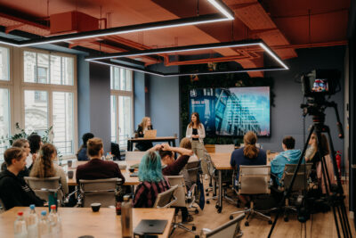 Start-ups der R42 Games Accelerator Klasse 2026 sitzen in einem Workshopraum an Gruppentischen, während Kim Steffen vorne die Tagesagenda präsentiert.