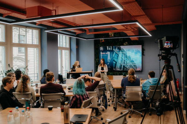 Start-ups der R42 Games Accelerator Klasse 2026 sitzen in einem Workshopraum an Gruppentischen, während Kim Steffen vorne die Tagesagenda präsentiert.