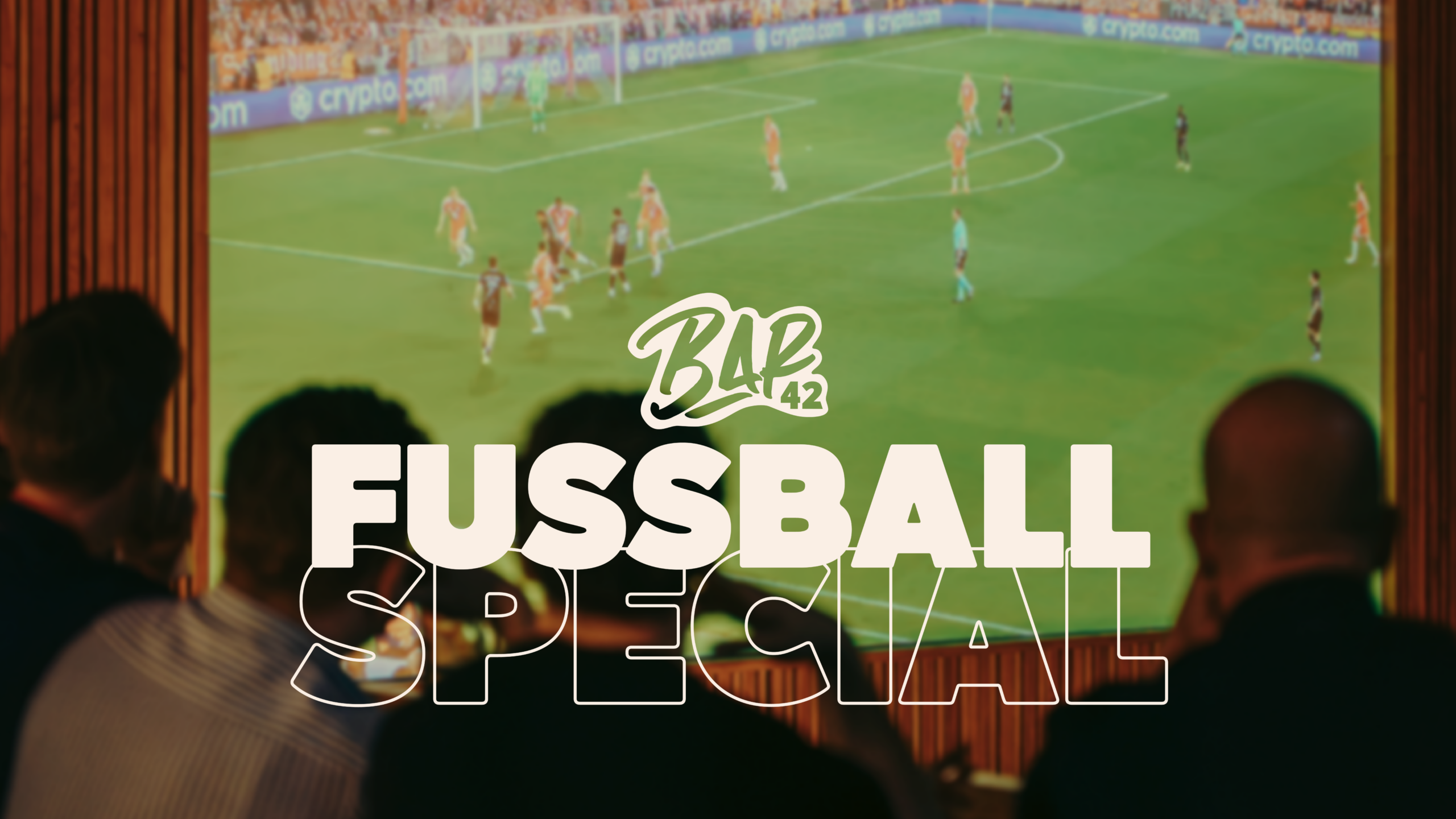 Blick in die Event Arena des R42. Auf der großen Leinwand läuft ein Fußballspiel. Davor sitzen mehrere Personen und sehen sich das Spiel an. Auf dem Foto ist Schrift: Bar42 Fußball Special